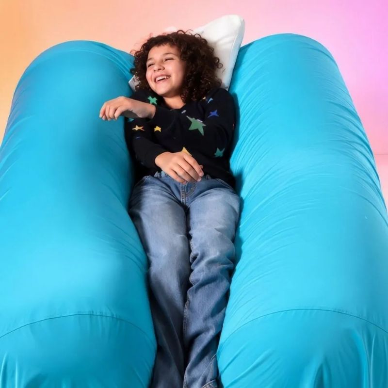 Laughing child lying between the two TFH Mega Squish & Squash Tubes, enjoying the body-weight "sandwich squish" for proprioceptive input and self-regulation