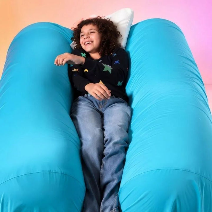 Laughing child lying between the two TFH Mega Squish & Squash Tubes, enjoying the body-weight "sandwich squish" for proprioceptive input and self-regulation