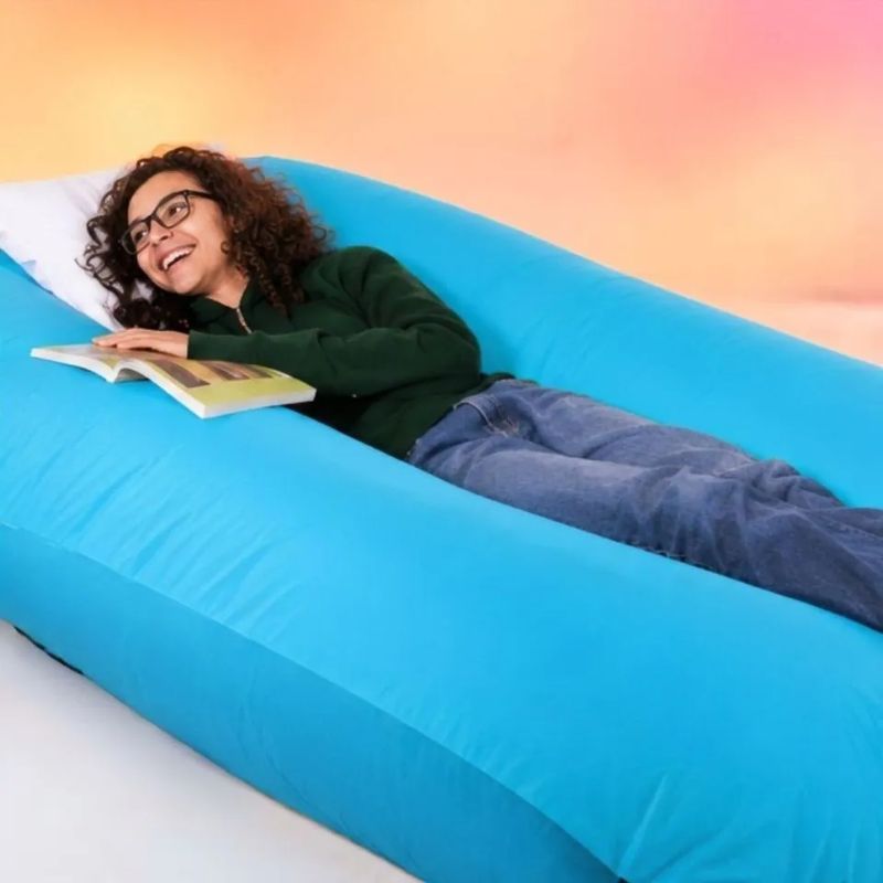 Smiling young woman reading a book while lying on the TFH Mega Squish & Squash Tubes, a soft velvet deep pressure tool for relaxation at home or in calm corners