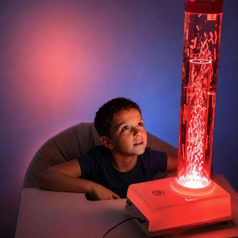 Boy gazing up at the TFH Tabletop Hurricane Tube Waterless glowing red, showing white beads swirling up the portable waterless sensory tube for calming visual tracking