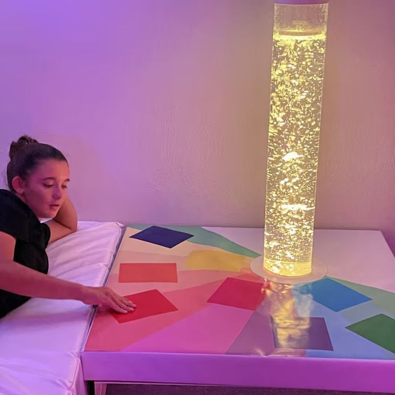 TFH Touch-A-Color Podium beside a bubble tube glowing gold, showing colour control in a calming sensory room