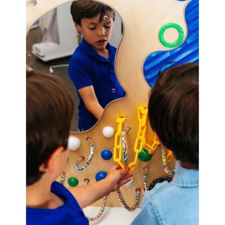 Child exploring the built-in mirror on the TFH Tranquil Textured Wall while another child reaches for the tactile chain feature, a sensory panel for classrooms and therapy rooms