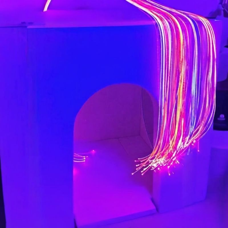TFH UV Fibre Optic Tails draped over a padded sensory den in a purple-lit room, the glowing strands cascading beside the doorway to create a calm sensory hideaway