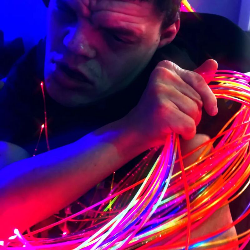 Man resting calmly while holding a bundle of glowing pink and orange TFH UV Fibre Optic Tails, safe-to-hold fibre optic strands for tactile and visual sensory input