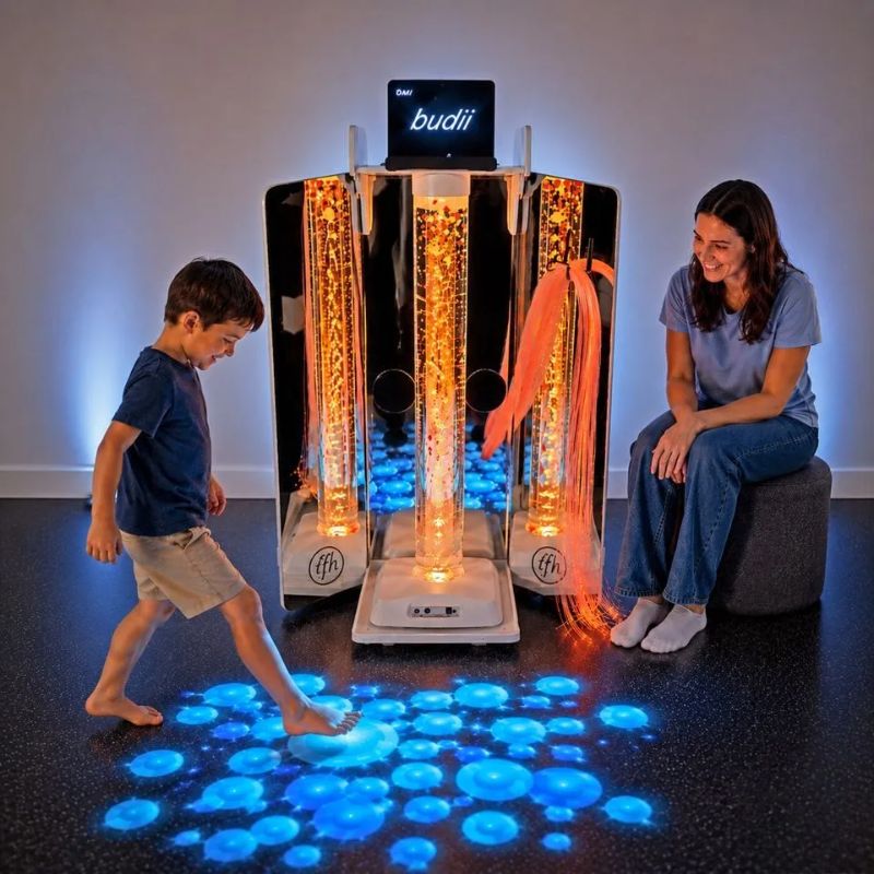 Child stepping onto blue bubbles projected by the TFH Vecta Budii Omi Budii system while an adult watches, the mobile sensory cart glowing orange behind them