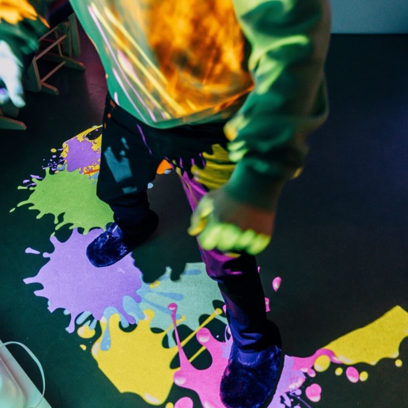 Child engaging in active play with the TFH Vecta Budii Omi Budii interactive projection system, viewed from above showing gesture-controlled sensory interaction