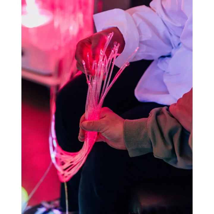 Hands exploring a bundle of pink-lit fibre optic tails from the TFH Vecta Budii mobile sensory cart, offering calming tactile and visual sensory input