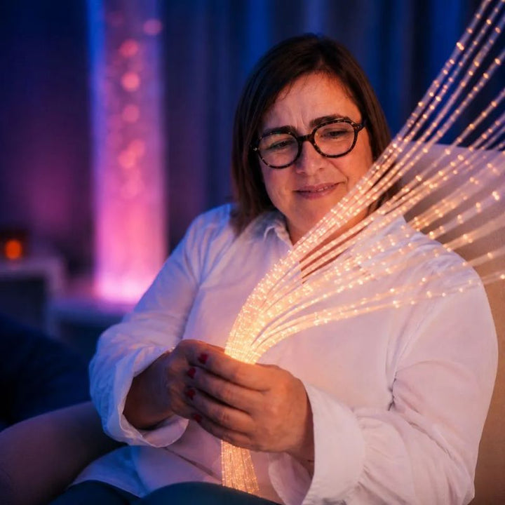 Woman gently holding a bundle of amber-lit strands from the TFH Wall Mounted Fiber Optic Curtain, the soft fibre optic tails safe to touch and explore by hand