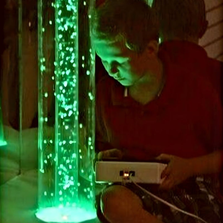 TFH Interactive Waterless Hurricane Tube with a child actively engaging with the 6-inch diameter snow bead sensory column, showing the colour-changing waterless bubble tube in use in a sensory room