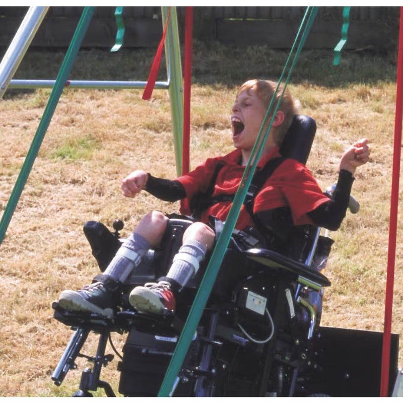 A boy in his wheelchair laughing while swinging on the TFH Wheelchair Platform Swing, an inclusive sensory swing for outdoor play