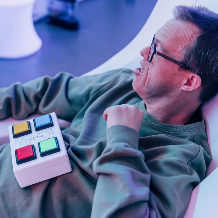 Man using the TFH 4-Button Wireless Colour Controller to control sensory room lighting from a reclined position