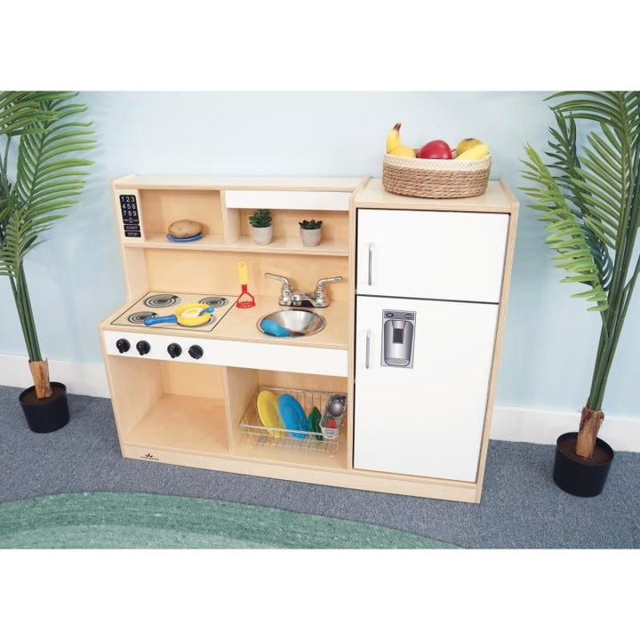 Whitney Brothers Let's Play Toddler Kitchen Combo in white, a wooden toddler play kitchen styled for dramatic play in a bright daycare classroom