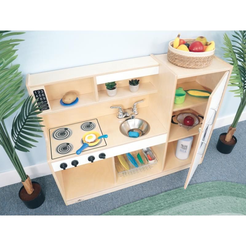 Open refrigerator on the Whitney Brothers Let's Play Toddler Kitchen Combo showing interior shelves, a toddler play kitchen with a full-length piano hinge door