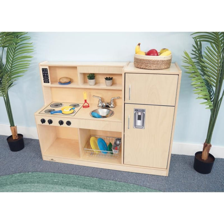 Whitney Brothers Let's Play Toddler Kitchen Combo in natural birch, a wooden toddler play kitchen with stove, sink and refrigerator set up for pretend play in a classroom