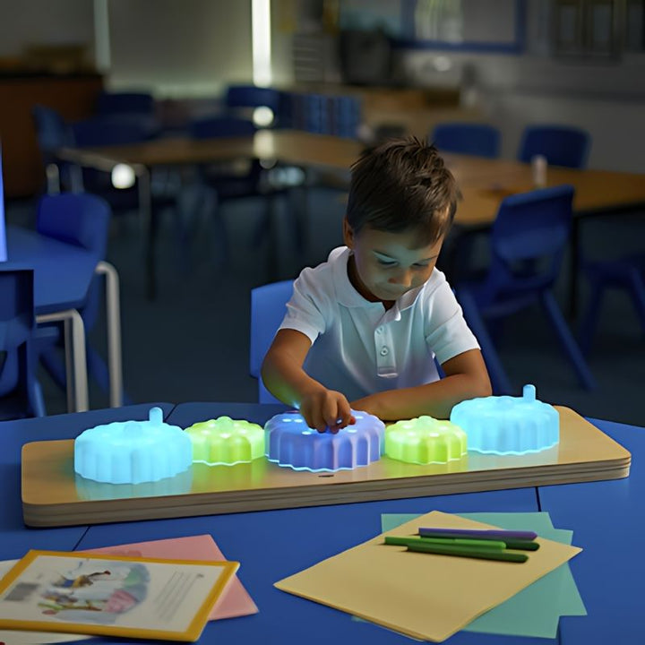 Boy playing with the TTS Light Up Cog Board on a blue table, engaging in cause-and-effect and fine motor skill development