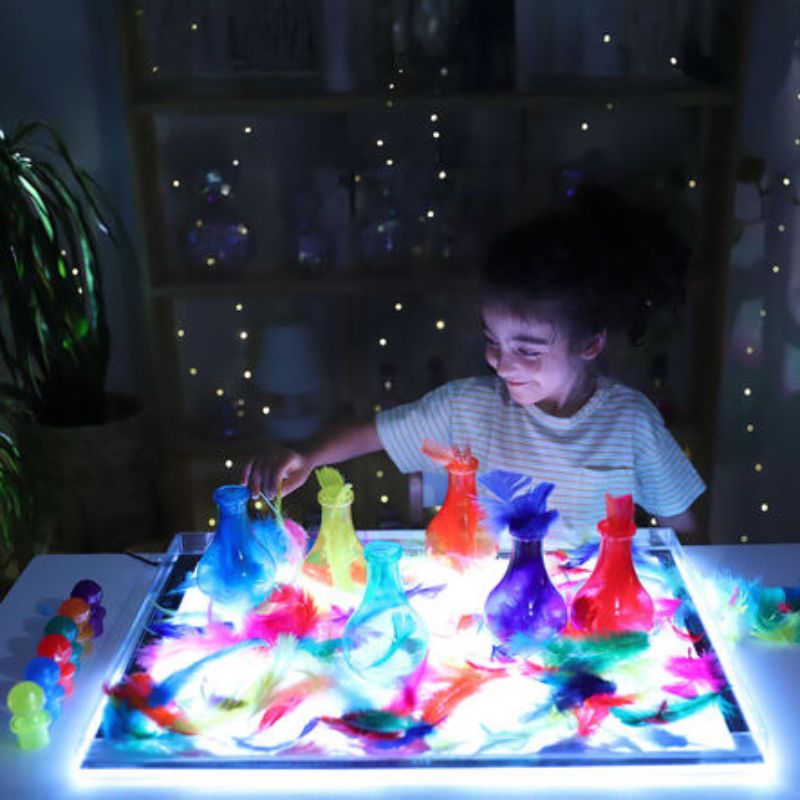 Child playing with coloured bottles and feathers on the TTS Colour Changing Light Panel, exploring transparency and colour through loose parts play