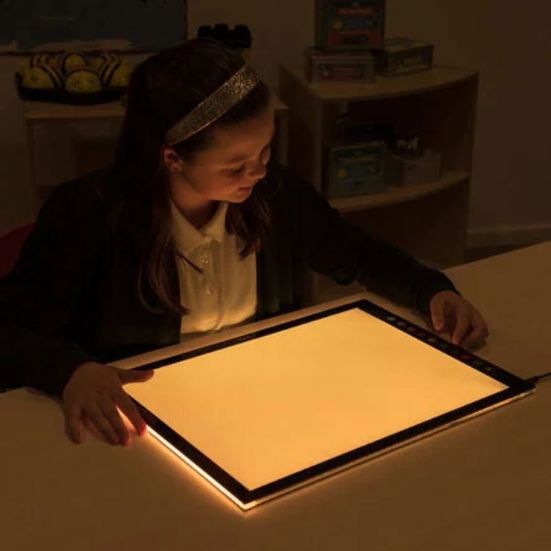 Girl using the TTS Colour Changing Light Panel in warm amber light mode, showing the adjustable LED surface for calm sensory and visual learning