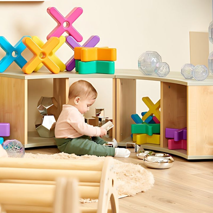 Baby exploring a Montessori-style early years classroom with TTS Glow Crosses and other sensory construction resources displayed on open shelving, showing classroom and nursery use