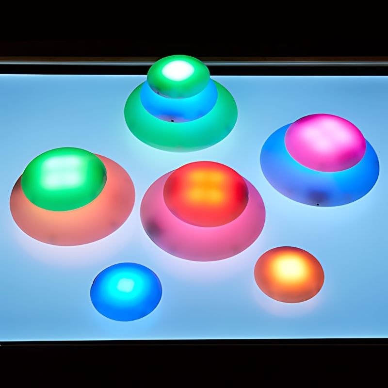 TTS Glow Pebbles set of 12 arranged in a landscape display, showing colour-changing LED illumination for sensory room and classroom use