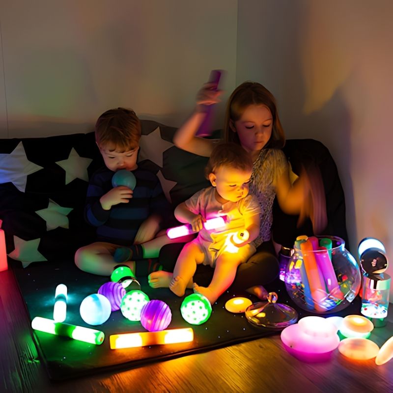 Three children engaged in collaborative light-up sensory play with the TTS Sensory Light Up Glow Collection, exploring glow cubes and rollers together
