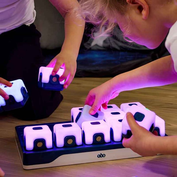 Two children removing TTS Glow Sequencing Cubes from the branded TTS charging dock, showing the rechargeable storage and distribution system for classroom use