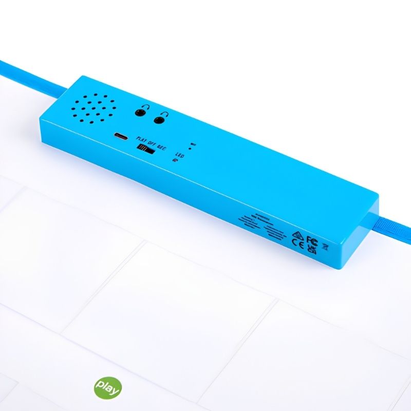 Angled view of the TTS Interactive Talking Mat blue audio unit showing the USB-C charging port, headphone sockets, speaker grille and product certification markings