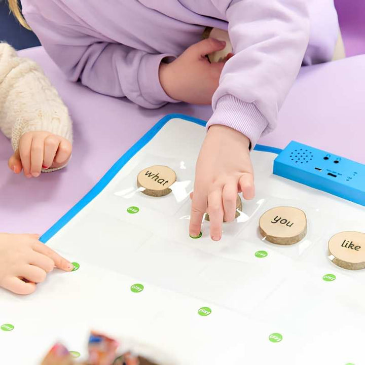 Two young children using the TTS Interactive Talking Mat on a classroom table, placing wooden word tokens into pockets to support speaking and language development