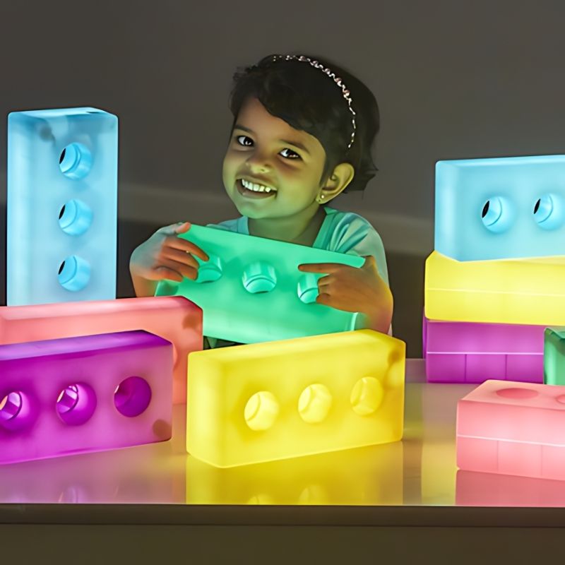 Young child holding and embracing TTS Light Up Glow Construction Bricks, demonstrating the toddler-friendly size and engaging sensory light play experience