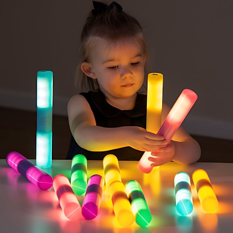 TTS Light Up Glow Cylinders arranged on a desk as a child plays, demonstrating LED sensory light exploration and fine motor engagement