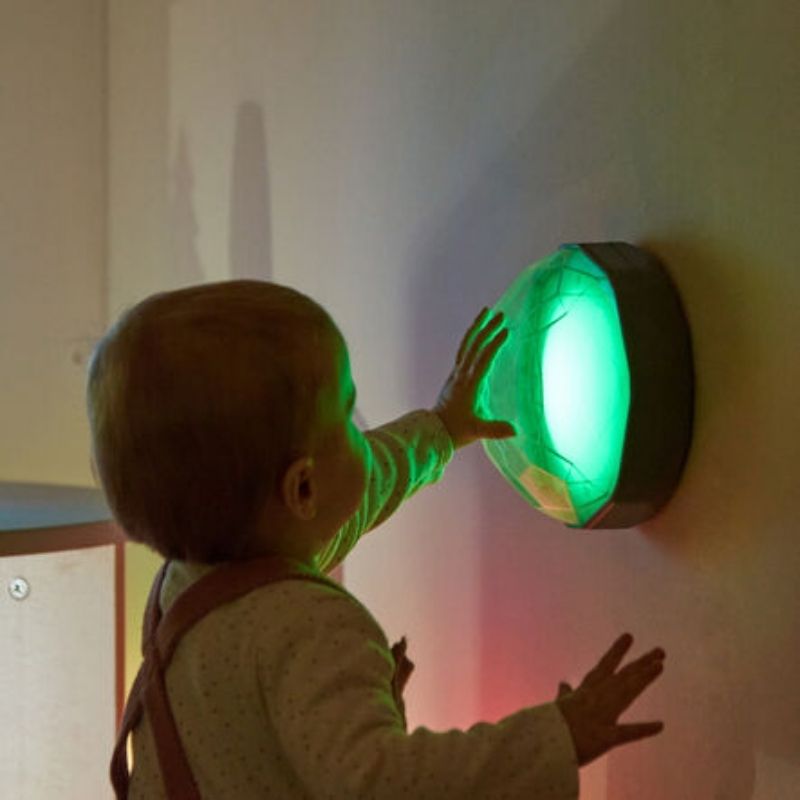 TTS Light Up Recordable Domes mounted on a wall glowing green, showing the LED colour-changing sensory light in active use by a child