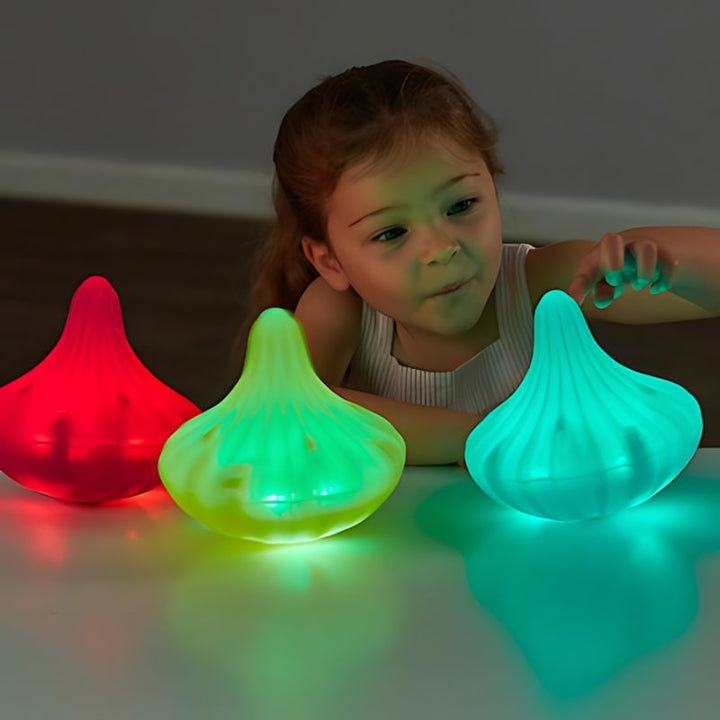 Young child captivated by three TTS Light Up Twist and Turn Spinning Tops glowing in red, green, and teal, demonstrating visual sensory stimulation and cause-and-effect exploration