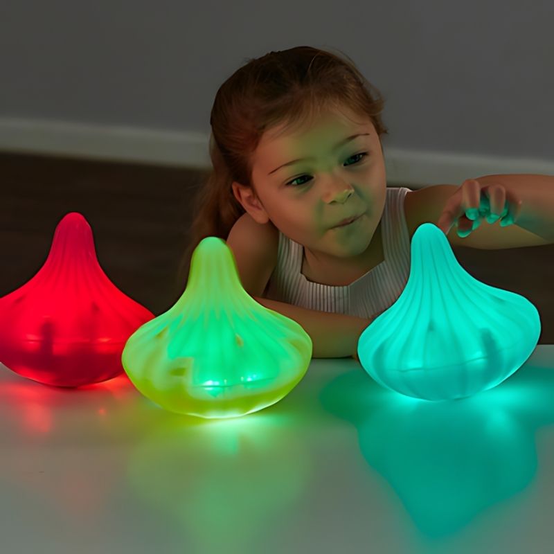 Young child captivated by three TTS Light Up Twist and Turn Spinning Tops glowing in red, green, and teal, demonstrating visual sensory stimulation and cause-and-effect exploration