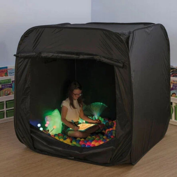 Girl drawing on a light panel inside the black TTS Pop-Up Sensory Space, set up as a ball pit with fibre optic lights for calm sensory play