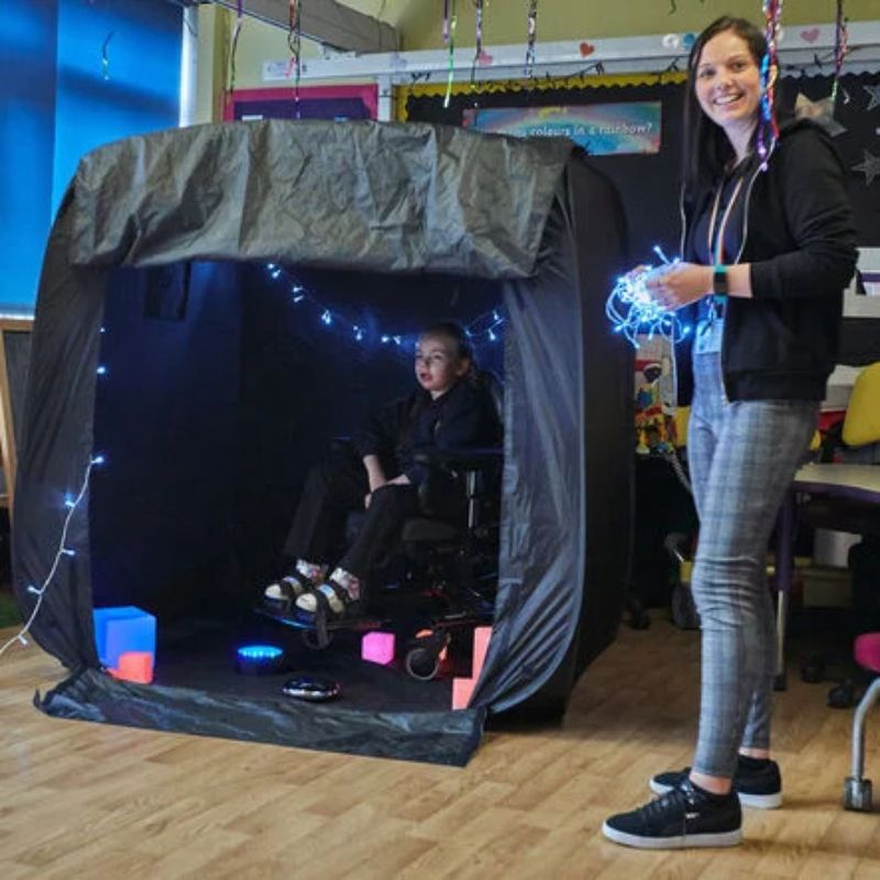 Child in a wheelchair inside the TTS Pop-Up Sensory Space decorated with fairy lights, showing the wide flush-to-floor entrance for accessible sensory play