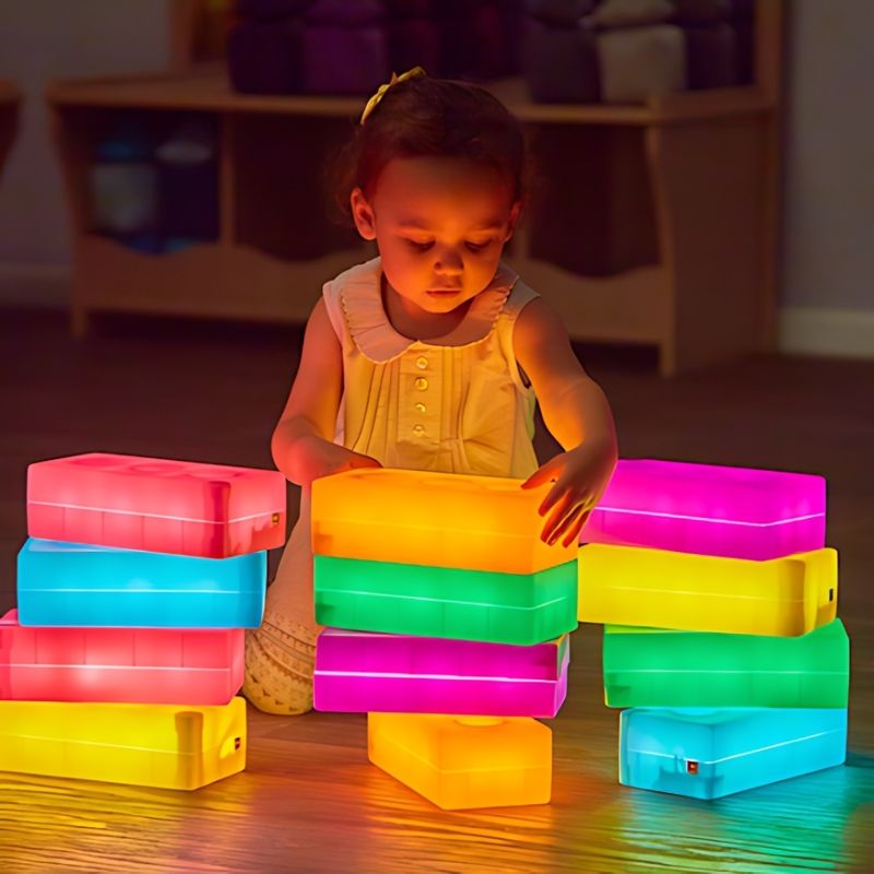 Child playing with a pile of TTS rechargeable glow construction bricks, supporting free exploration, fine motor skills, and tactile sensory development