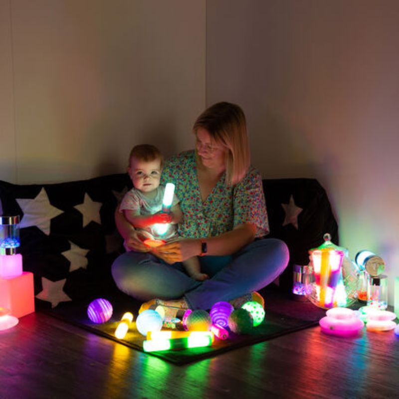 Adult and baby sharing calm sensory play with the TTS Sensory Light Up Glow Collection, the baby holding a glowing light stick surrounded by colourful light-up balls and jars