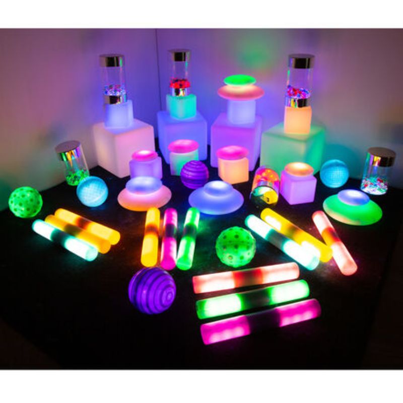 TTS Sensory Light Up Glow Collection laid out in full, with glowing cubes, discs, textured balls, light sticks and sensory jars in bright colour-changing light