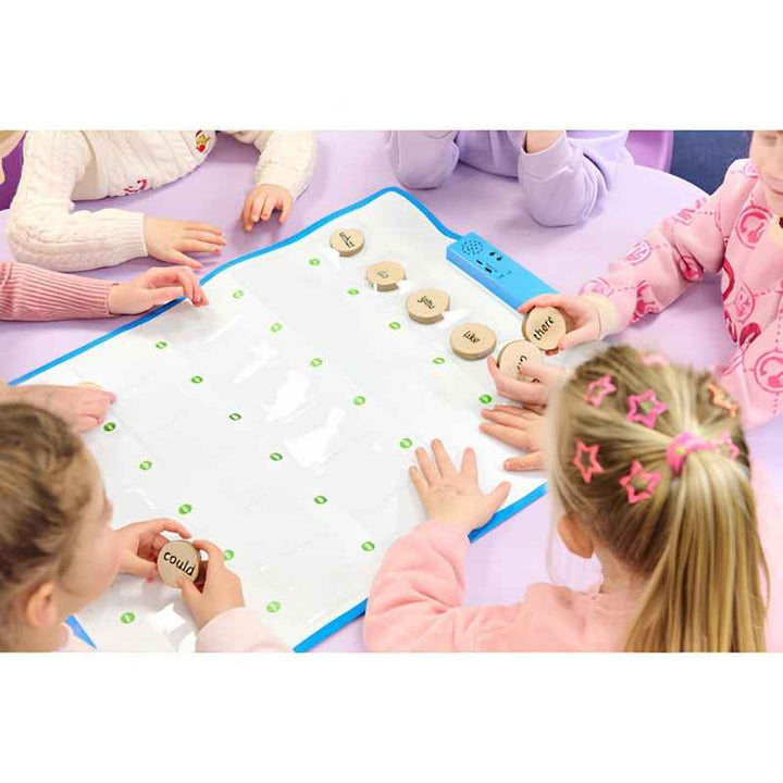 A group of young children seated on the floor using the TTS Interactive Talking Mat for a collaborative floor-based speaking and language activity with wooden word tokens