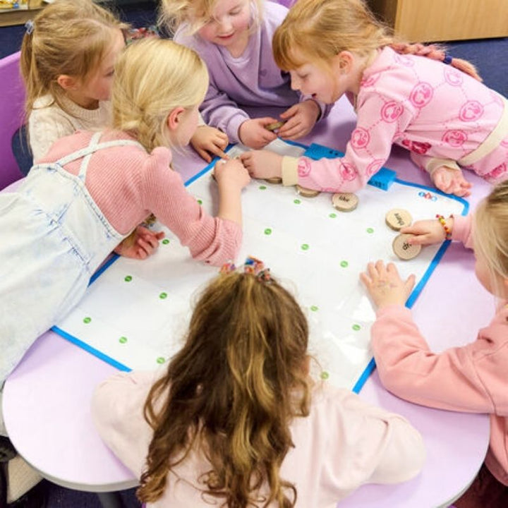 A group of children collaborating around the TTS Interactive Talking Mat in a classroom setting, using wooden word tokens for a shared spoken language and communication activity