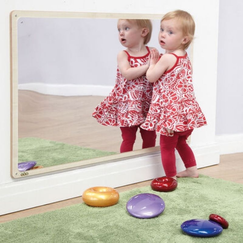TTS Wooden Framed Toddler Mirror with a toddler standing and engaging with her reflection, demonstrating the mirror's ideal wall-mounted height for early years use