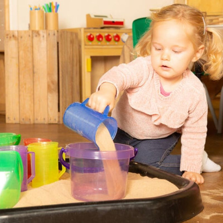 Girl playing with TTS Translucent Colour Bucket Set in sand, developing stacking, sorting, and fine motor skills through open-ended sensory exploration