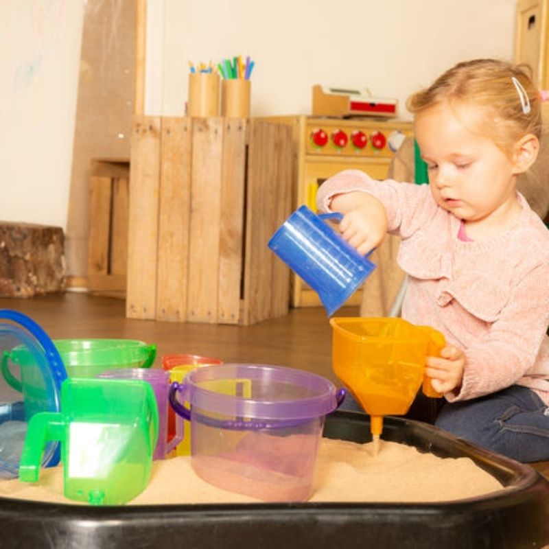 Girl exploring with TTS Translucent Colour Bucket Set in a sensory sand tray, building tactile awareness and developmental skills through hands-on play