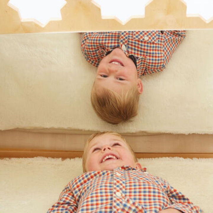 Toddler boy laughing at his reflection in the mirrored side of the TTS Wooden Pyramid Den, supporting early self-awareness and visual processing