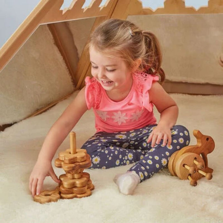 Girl stacking wooden toys inside the TTS Wooden Pyramid Den, using the cosy enclosed space as a calm corner for focused play