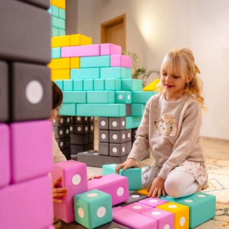 Two children actively building a floor-scale structure with the TUKI BIG Magnetic Blocks Builder 110, showing the collaborative large-format 10cm foam block construction the 110-piece group set supports