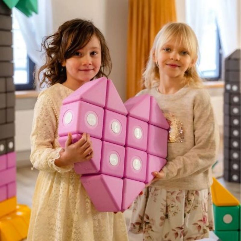 Two girls collaboratively building a heart figure with the TUKI BIG Magnetic Blocks Builder 128, demonstrating the voluntary collaborative pair dynamic that emerges when 128 blocks provides full personal block access for every child in a 7-10 child group