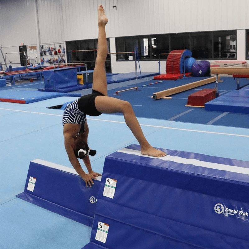 Gymnast performing a back bend on the Tumbl Trak Pyramid Beam Blocks, showing the stable trapezoid foam surface supporting advanced gymnastics skill progressions including back walkovers and flexibility training for all levels