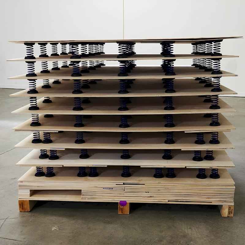 Tumbl Trak semi-assembled spring floor panels stacked on a shipping pallet with high-carbon steel springs and purple retainer caps visible between layers, ready for delivery to gymnastics and cheer facilities