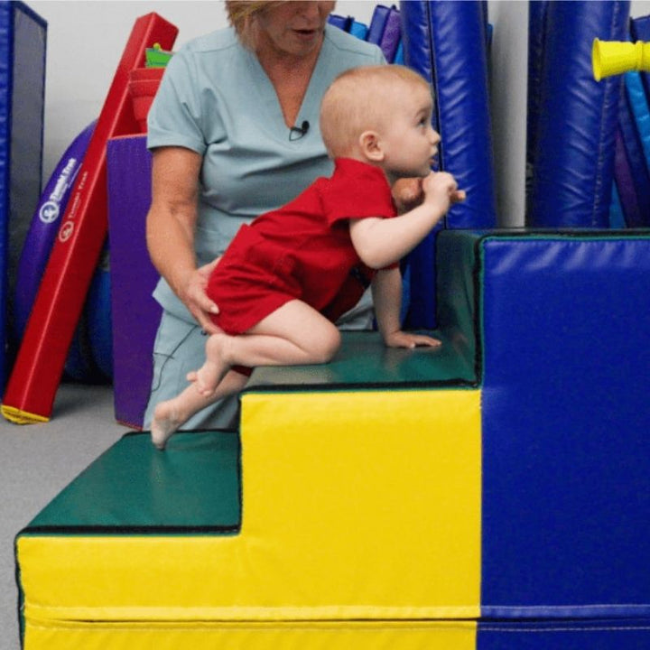 Child actively stepping up the Tumbl Trak Steps foam gymnastics access block, demonstrating gross motor development, balance, and the gradual three-step approach to elevated gymnastics and movement training equipment