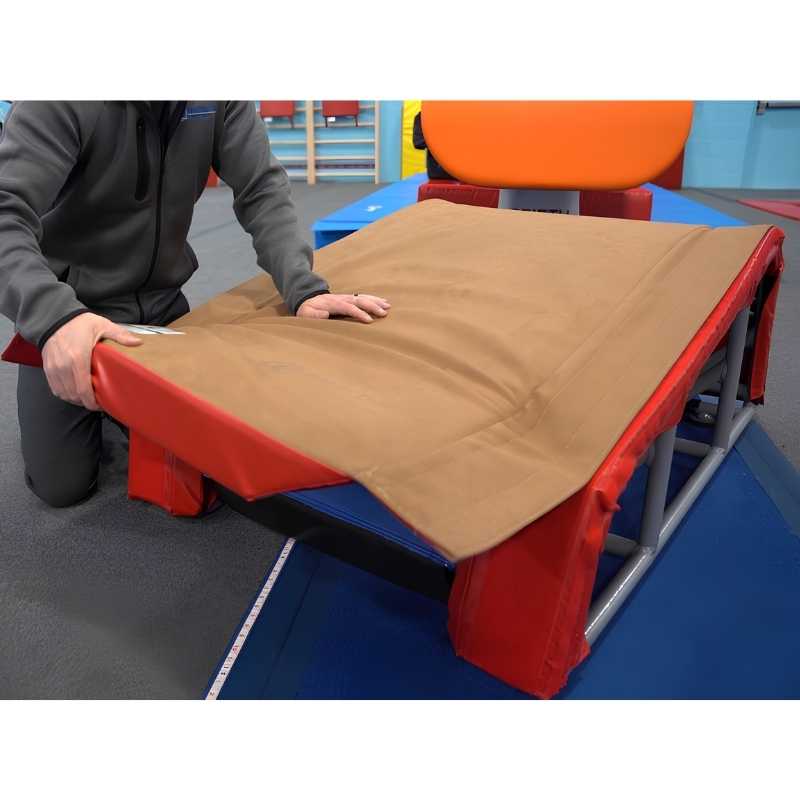 Coach attaching the Tumbl Trak T-Trainer Cover PRO suede vault topper to the T-Trainer in a gymnastics gym setting, demonstrating the quick Velcro installation process